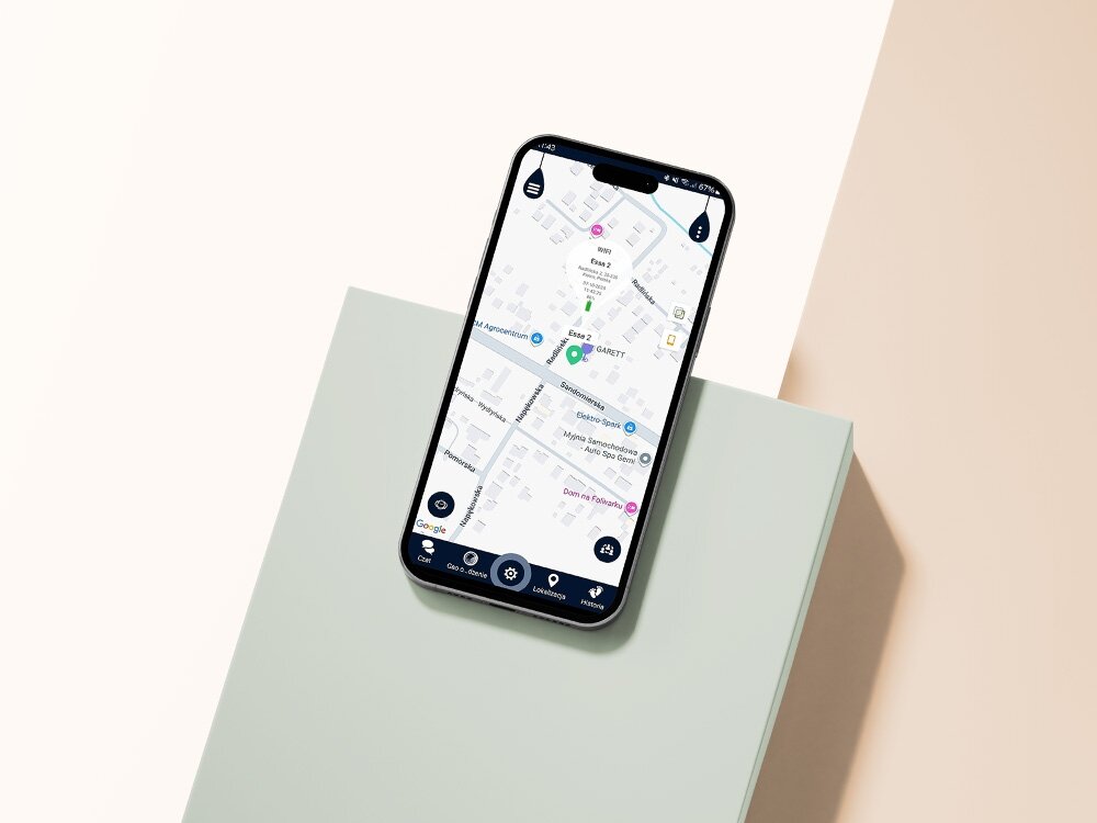 Smartfon z wyświetloną mapą na ekranie, leży na jasnej powierzchni. Na mapie widoczne są różne punkty i ulice, w tym oznaczenie \'GARETT\'.