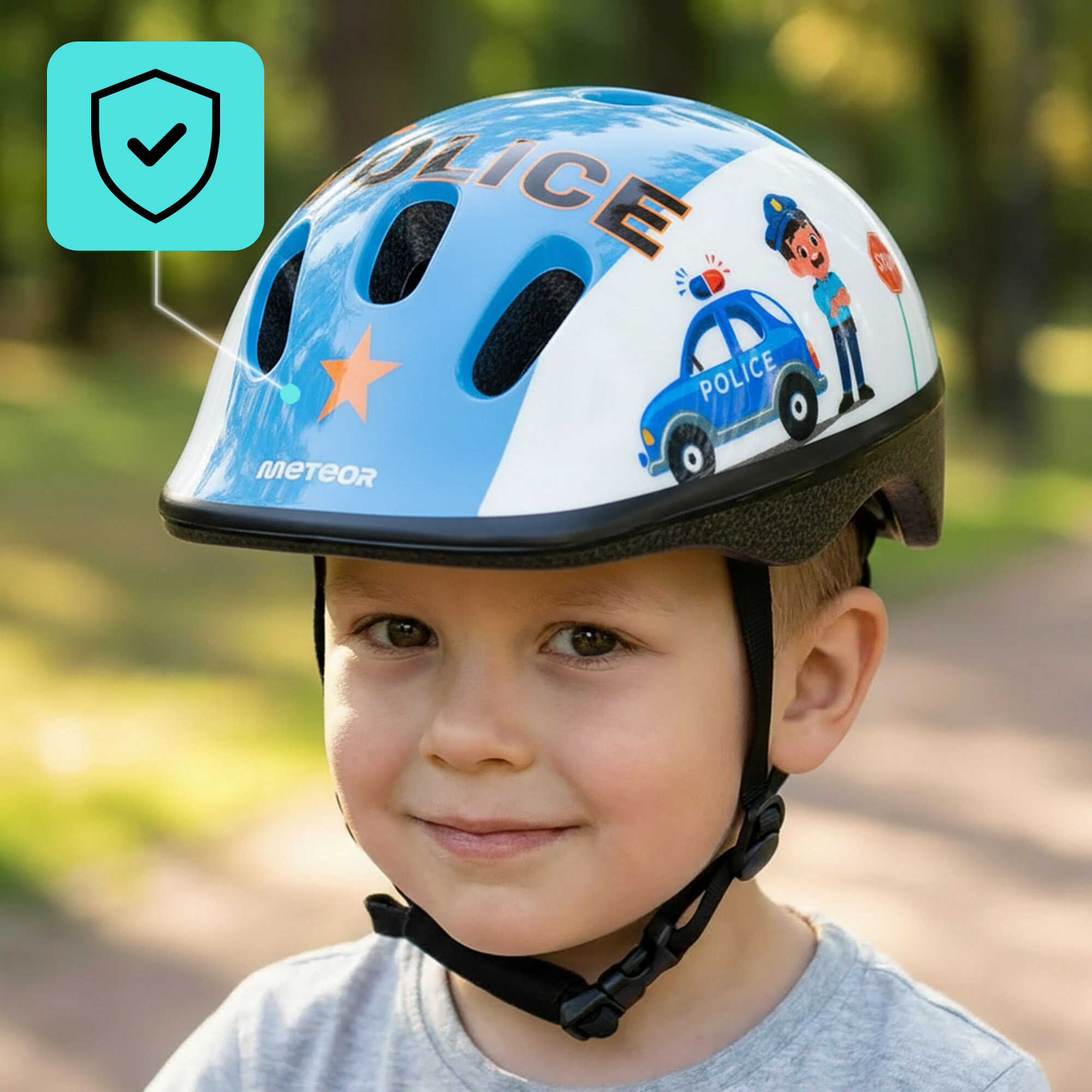 Dziecko nosi kask rowerowy z motywem policyjnym, z napisem \'POLICE\' i grafiką samochodu policyjnego oraz postacią policjanta. Na kasku widoczne jest logo \'METEOR\'.