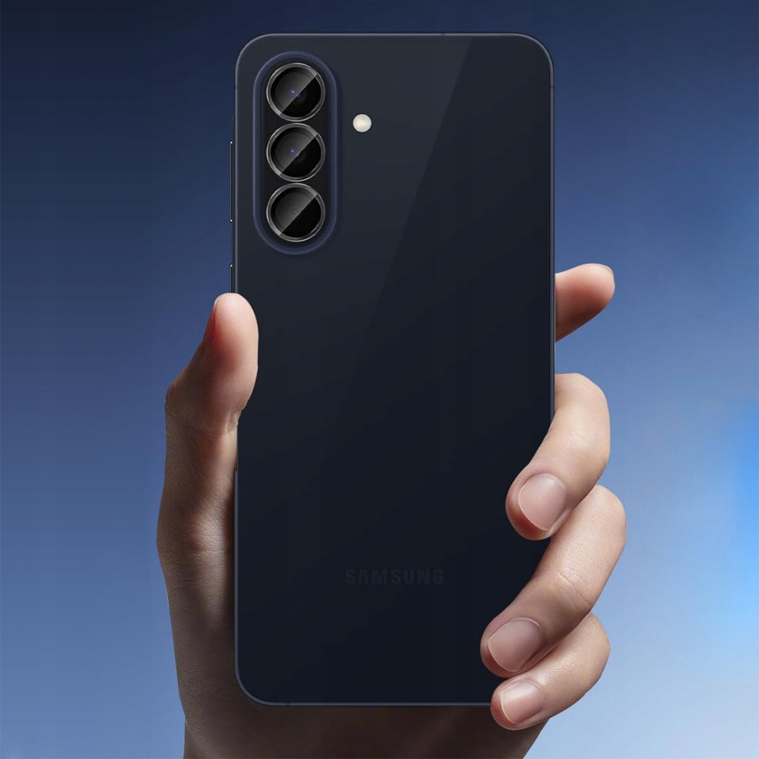 Osoba trzyma smartfon z trzema obiektywami aparatu i lampą błyskową na tylnej obudowie. Na dole widoczny jest napis \'SAMSUNG\'.