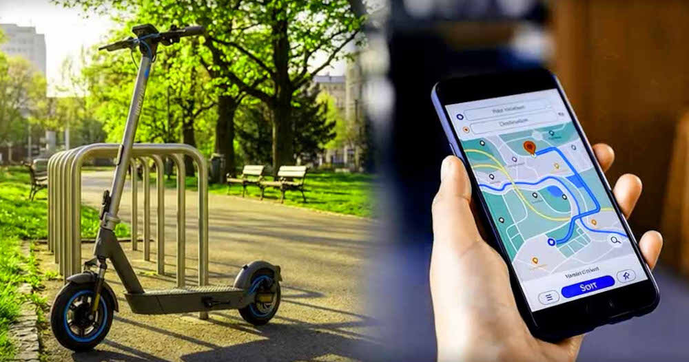 Na obrazie widać elektryczną hulajnogę stojącą na ścieżce w parku oraz dłoń trzymającą smartfon z aplikacją mapy. Hulajnoga jest szaro-turkusowa, a w tle znajdują się drzewa i ławki.