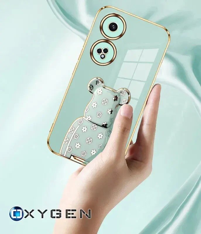 Osoba trzyma etui na telefon z motywem misia i kwiatów, z widocznymi otworami na aparat. Na dole widoczne jest logo \'OXYGEN\'.