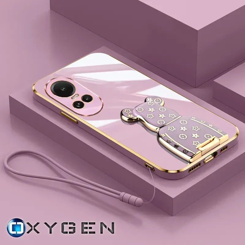Na obrazie widoczne jest różowe etui na telefon z ozdobnym uchwytem w kształcie misia, ozdobionym gwiazdkami i kółkami. W dolnej części znajduje się logo \'OXYGEN\' oraz przymocowana smycz.