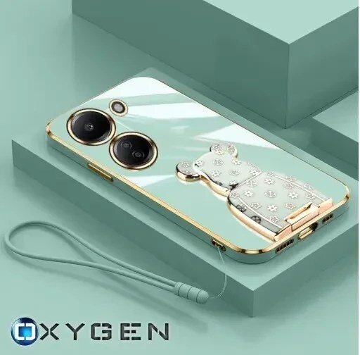 Etui na telefon z dwoma dużymi obiektywami aparatu i ozdobnym uchwytem w kształcie misia. Na dole widoczna jest smycz, a w lewym dolnym rogu logo OXYGEN.