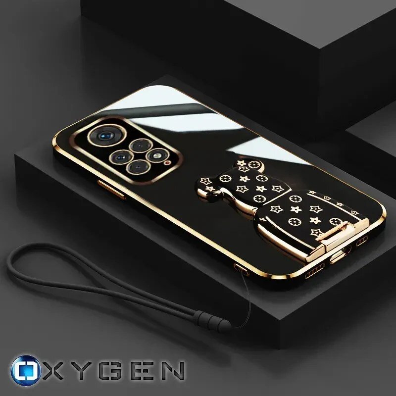 Na obrazie widoczne jest eleganckie etui na telefon z metalicznymi elementami i uchwytem w kształcie misia z wzorami. W dolnym rogu znajduje się logo \'OXYGEN\'.