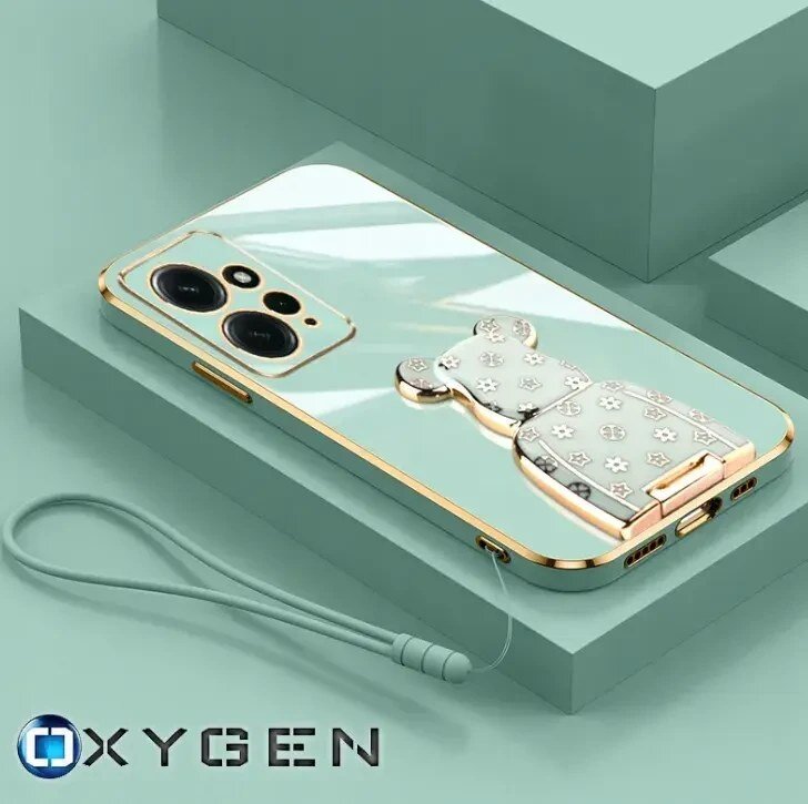 Etui na telefon z lustrzaną powierzchnią i złotymi krawędziami, ozdobione uchwytem w kształcie misia z wzorem gwiazdek. Na dole widoczny jest napis \'OXYGEN\'.