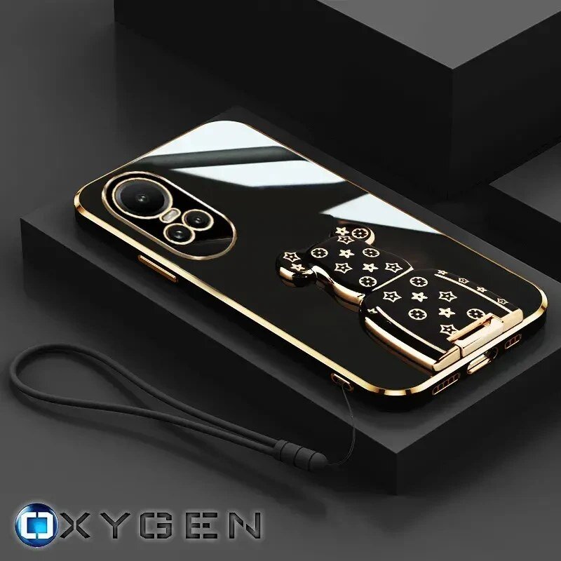 Na obrazie widoczne jest eleganckie etui na telefon z metalicznymi elementami i uchwytem w kształcie misia z wzorami. W dolnym rogu znajduje się logo \'OXYGEN\'.