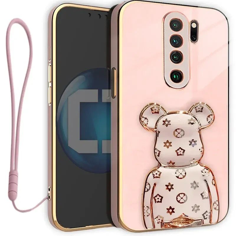 Etui na telefon w kolorze różowym z ozdobnym uchwytem w kształcie misia z wzorami. Obok znajduje się różowa smycz do telefonu.