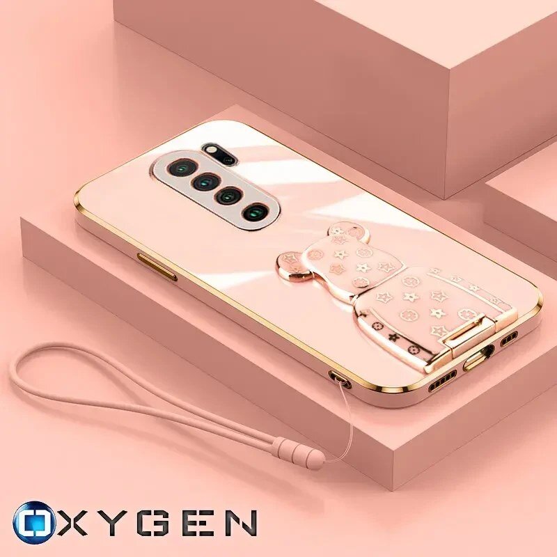 Różowe etui na telefon z uchwytem w kształcie misia, ozdobione gwiazdkami i serduszkami, leży na różowym tle. Widoczny jest również napis \'OXYGEN\' oraz smycz przymocowana do etui.
