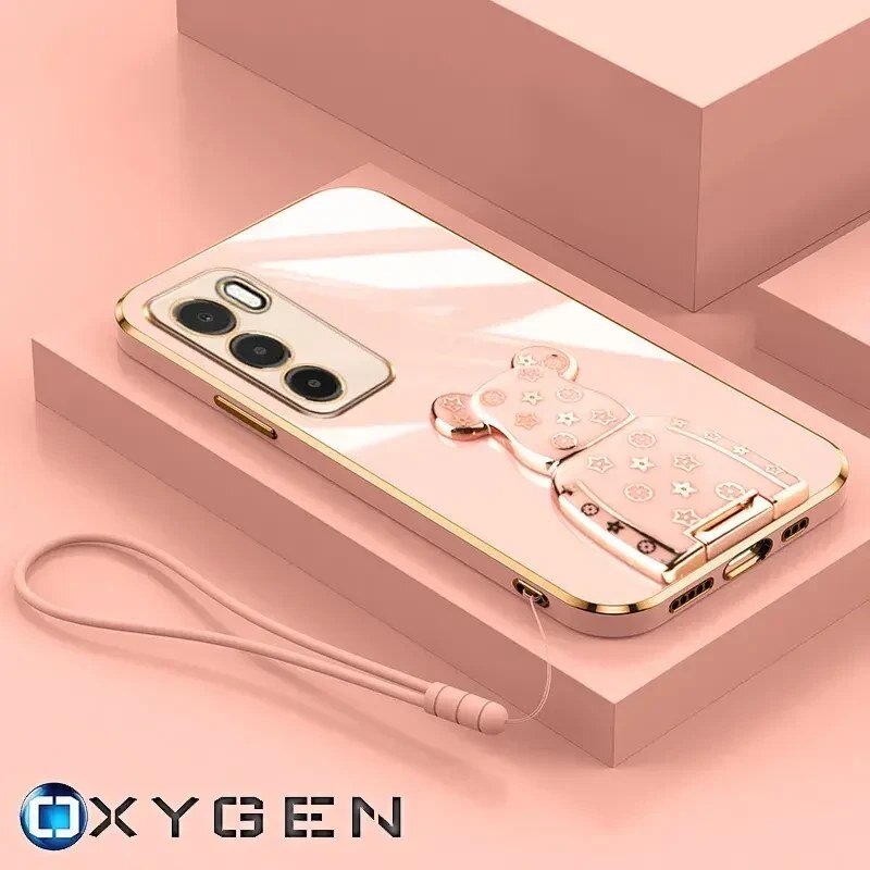Na obrazie widoczne jest różowe etui na telefon z uchwytem w kształcie misia, leżące na różowej powierzchni. W dolnym rogu znajduje się logo \'OXYGEN\'.