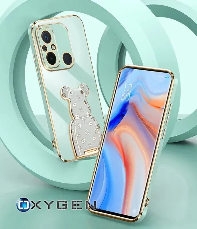 Na obrazie widoczne są dwa telefony w etui z przezroczystym tyłem i złotymi krawędziami, jeden z nich ma uchwyt w kształcie misia. W dolnym rogu znajduje się logo \'OXYGEN\'.