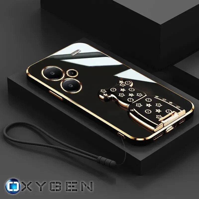 Na obrazie widoczne jest eleganckie etui na telefon z metalicznymi elementami i uchwytem w kształcie misia z wzorami. W dolnym rogu znajduje się logo \'OXYGEN\'.