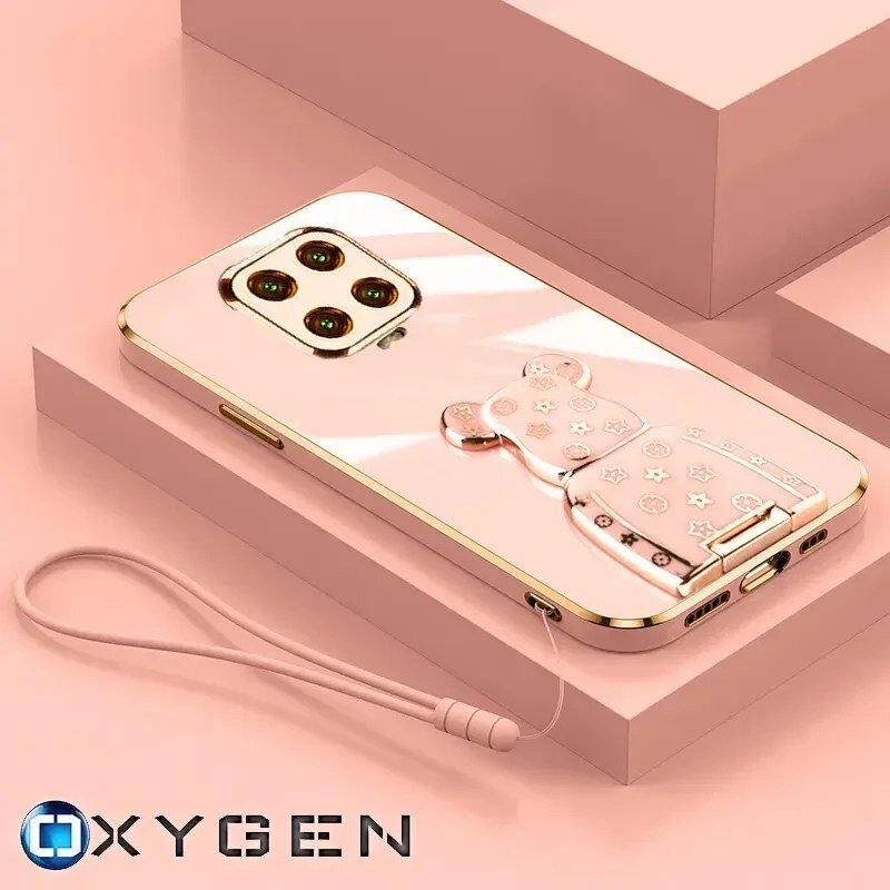 Na obrazie widoczne jest różowe etui na telefon z uchwytem w kształcie misia, ozdobionym gwiazdkami i innymi symbolami. W dolnej części zdjęcia znajduje się logo \'OXYGEN\'.