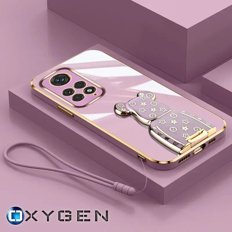 Na obrazie widoczne jest różowe etui na telefon z metalicznymi elementami i uchwytem w kształcie misia. W dolnym rogu znajduje się logo OXYGEN.