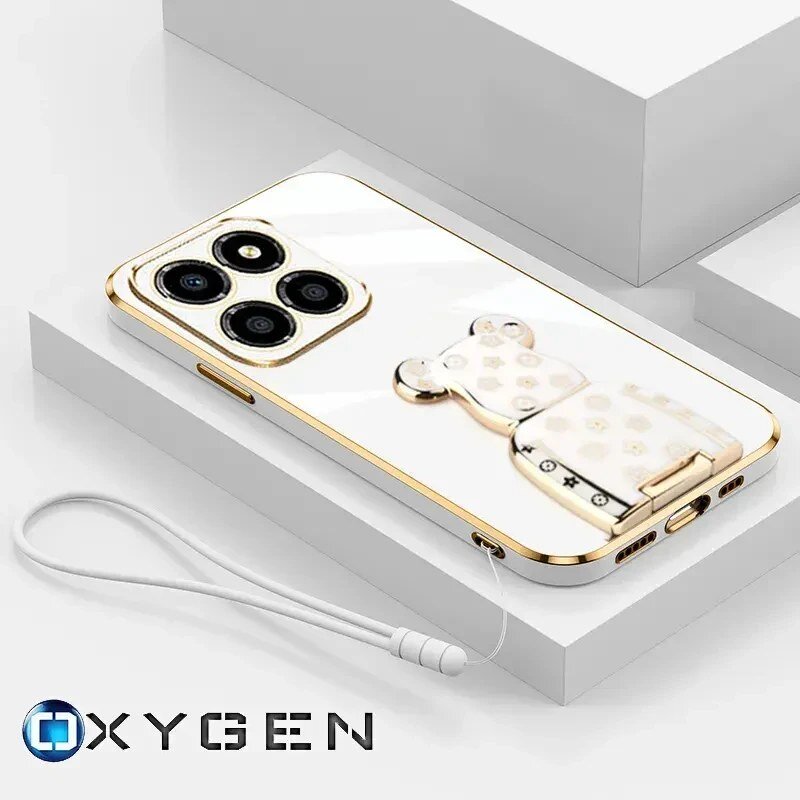 Na obrazie widoczne jest eleganckie etui na telefon z metalicznymi akcentami i ozdobnym uchwytem w kształcie misia. W dolnej części znajduje się logo \'OXYGEN\'.