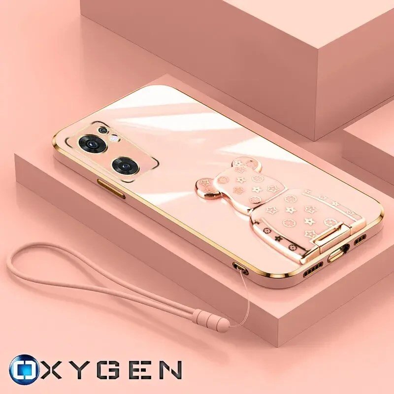 Różowe etui na telefon z metalicznym uchwytem w kształcie misia, ozdobionym gwiazdkami i kwiatkami. Na dole widoczny jest napis \'OXYGEN\'.