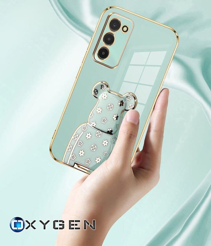 Osoba trzyma przezroczyste etui na telefon z ozdobnym wzorem misia i złotymi akcentami wokół aparatu. Na dole widoczne jest logo \'OXYGEN\'.