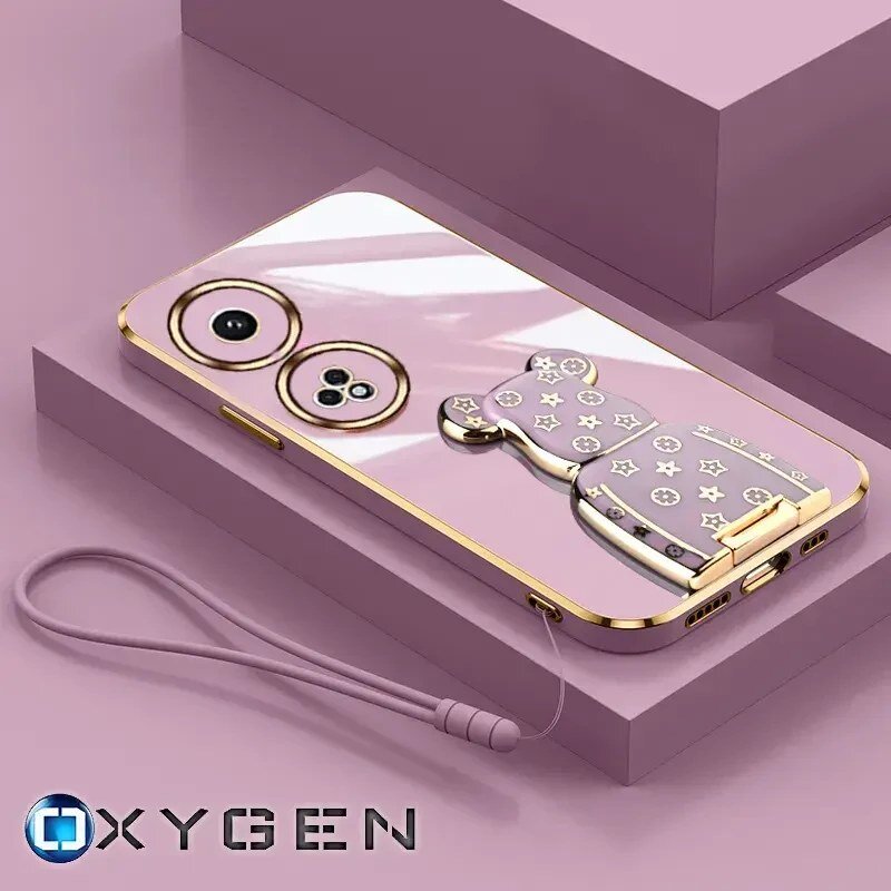 Różowe etui na telefon z metalicznymi elementami i uchwytem w kształcie misia, leży na różowym tle. Widoczne logo: OXYGEN.