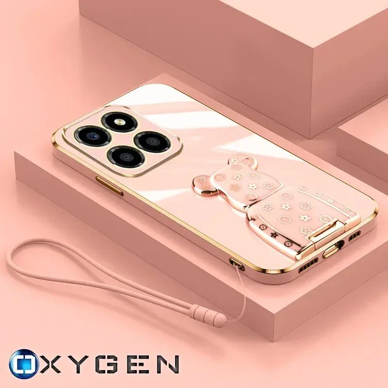 Na obrazie widoczne jest różowe etui na telefon z ozdobnym uchwytem w kształcie misia oraz smyczą. W dolnym rogu znajduje się logo OXYGEN.