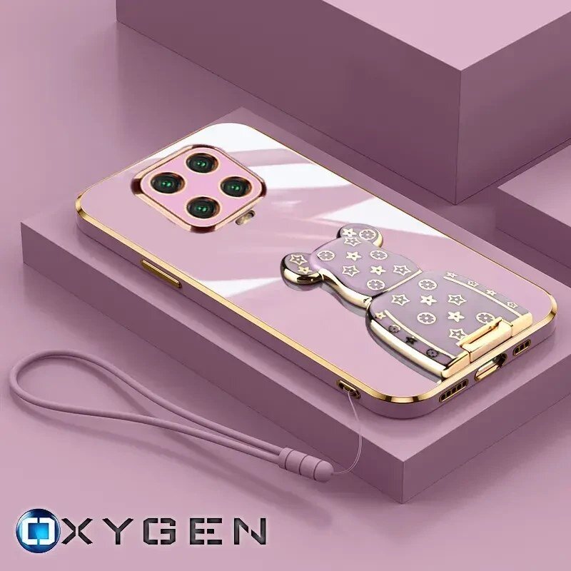 Na obrazie widoczne jest różowe etui na telefon z ozdobnym uchwytem w kształcie misia, ozdobionym gwiazdkami i kwiatkami. W dolnym rogu znajduje się logo \'OXYGEN\'.