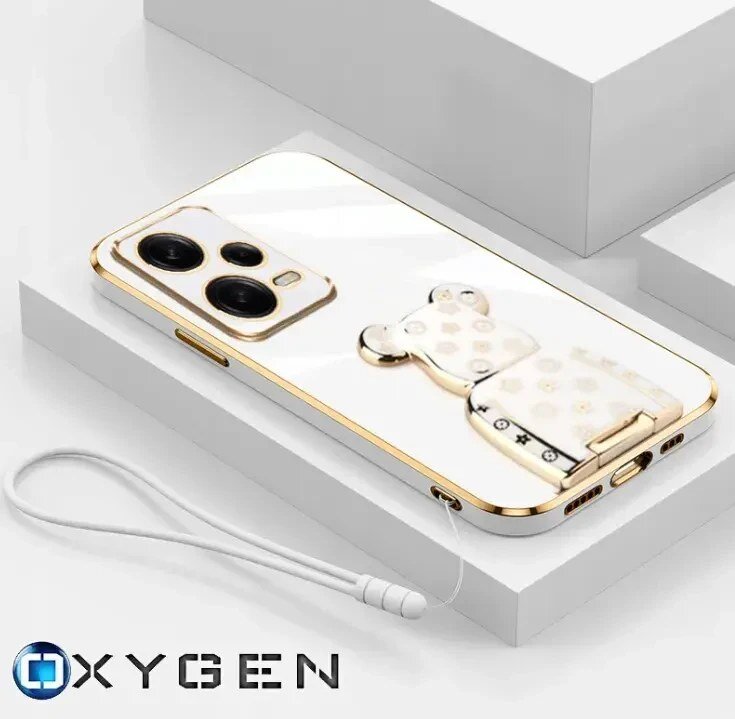 Na obrazie widoczne jest eleganckie etui na telefon z metalicznymi akcentami i uchwytem w kształcie misia. W dolnym rogu znajduje się logo \'OXYGEN\'.