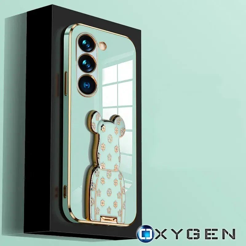 Etui na telefon z trzema widocznymi obiektywami aparatu i ozdobnym uchwytem w kształcie misia. Na dole obrazu znajduje się logo \'OXYGEN\'.