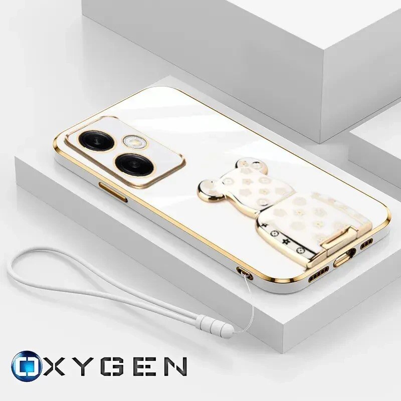 Na obrazie widoczne jest etui na telefon z ozdobnym uchwytem w kształcie misia, umieszczone na białym tle. W dolnym rogu znajduje się logo \'OXYGEN\'.