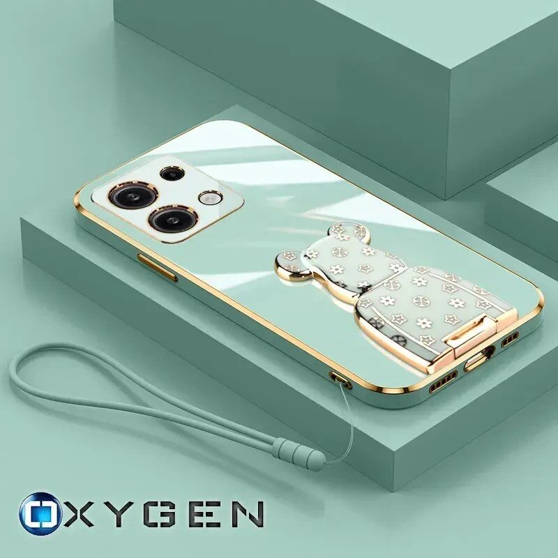 Na obrazie widoczne jest etui na telefon w kolorze miętowym z ozdobnym uchwytem w kształcie misia. W dolnej części znajduje się logo \'OXYGEN\'.