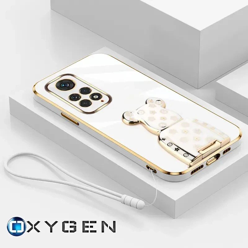 Na obrazie widoczne jest etui na telefon z ozdobnym uchwytem w kształcie misia oraz smyczą. W dolnym rogu znajduje się logo \'OXYGEN\'.