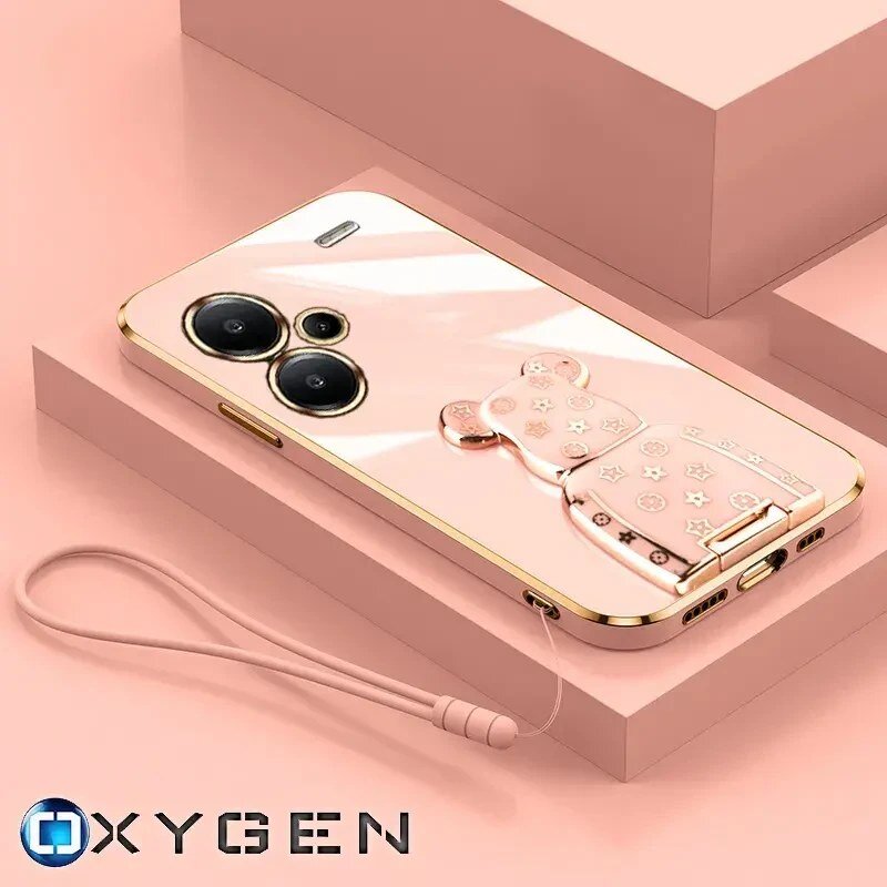 Na obrazie widoczne jest różowe etui na telefon z ozdobnym uchwytem w kształcie misia oraz smyczą. W dolnym rogu znajduje się logo \'OXYGEN\'.