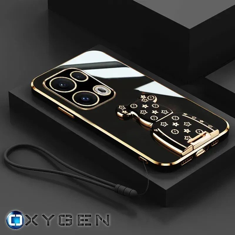 Na obrazie widoczne jest eleganckie etui na telefon z czarnym, błyszczącym wykończeniem i złotymi elementami, w tym uchwytem w kształcie misia z wzorem gwiazdek. W dolnym rogu znajduje się logo \'OXYGEN\'.