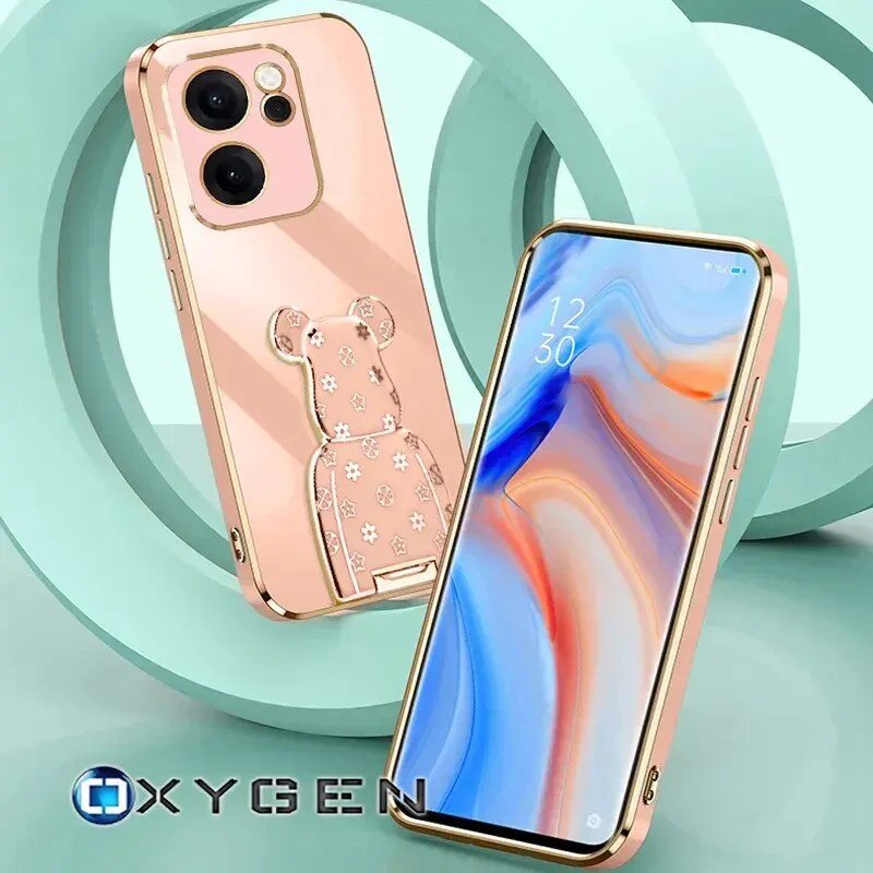Obraz przedstawia różowe etui na telefon z ozdobnym uchwytem w kształcie misia z wzorami. Na dole widoczne jest logo \'OXYGEN\'.