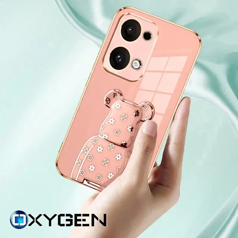 Osoba trzyma telefon w różowym etui z ozdobnym wzorem misia. Na dole widoczne jest logo OXYGEN.