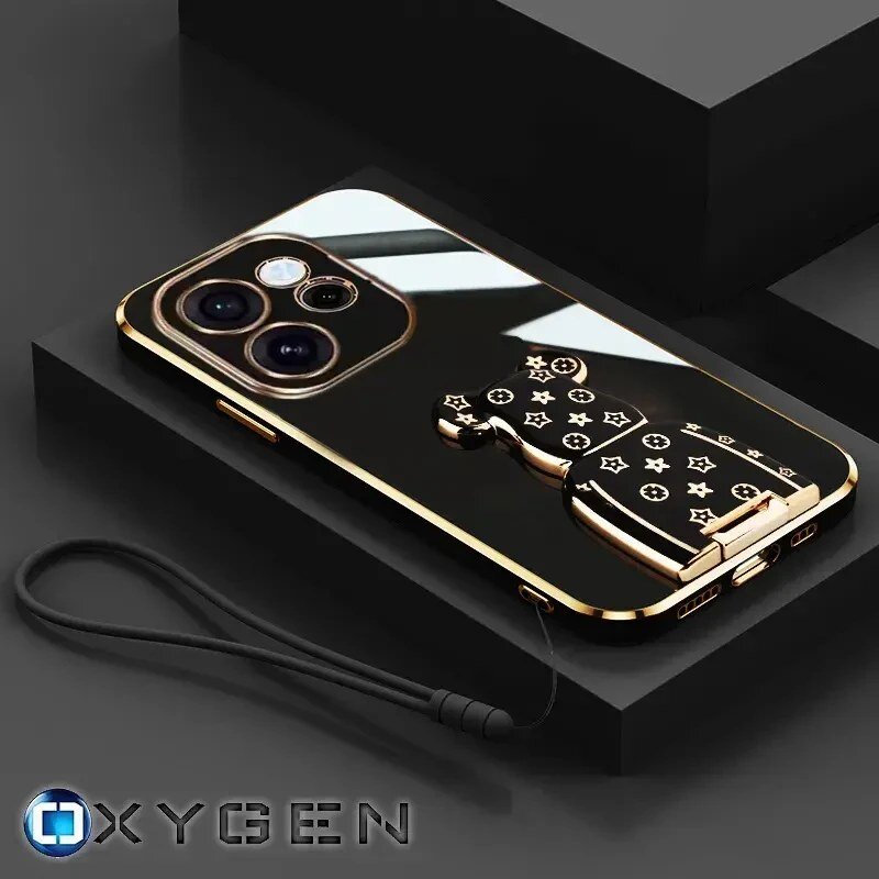 Na obrazie widoczne jest eleganckie etui na telefon z metalicznymi elementami i uchwytem w kształcie misia z wzorami. W dolnym rogu znajduje się logo \'OXYGEN\'.