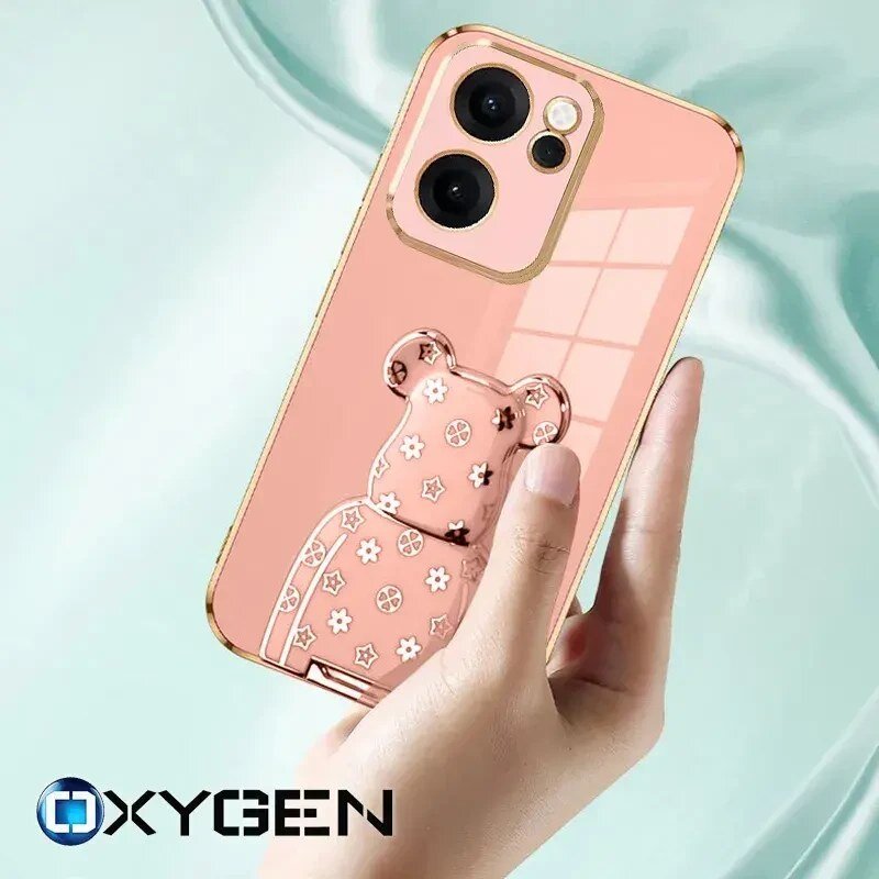 Osoba trzyma telefon w różowym etui z ozdobnym wzorem misia. Na dole widoczne jest logo OXYGEN.