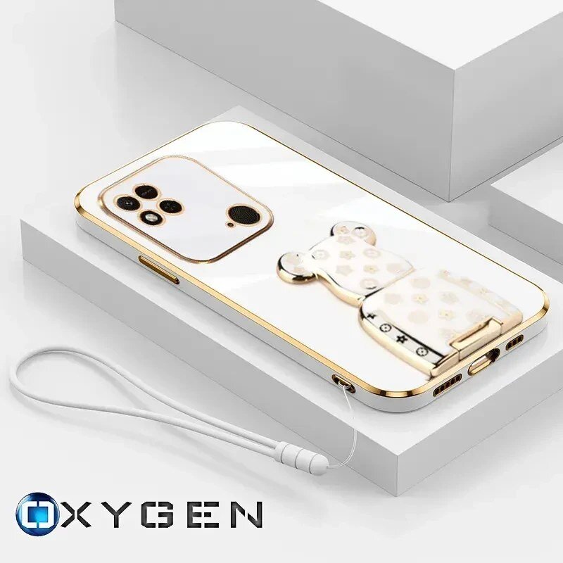 Na obrazie widoczne jest eleganckie etui na telefon z metalicznymi akcentami i ozdobnym uchwytem w kształcie misia. W dolnej części obrazu znajduje się logo \'OXYGEN\'.