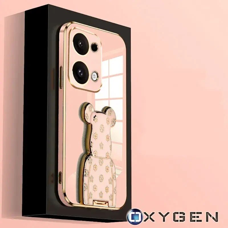 Etui na telefon w kolorze różowego złota z uchwytem w kształcie misia, ozdobionym wzorami. W prawym dolnym rogu widoczne jest logo \'OXYGEN\'.