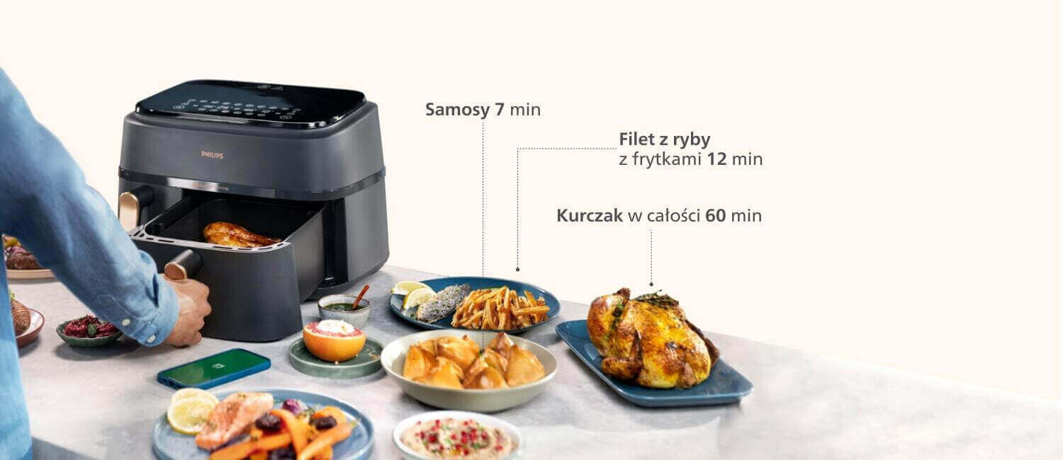 Na obrazie widoczna jest frytkownica beztłuszczowa z otwartym koszem, w którym znajduje się jedzenie. Obok frytkownicy znajdują się talerze z różnymi potrawami oraz tekst: \'Samosy 7 min\', \'Filet z ryby z frytkami 12 min\', \'Kurczak w całości 60 min\'.