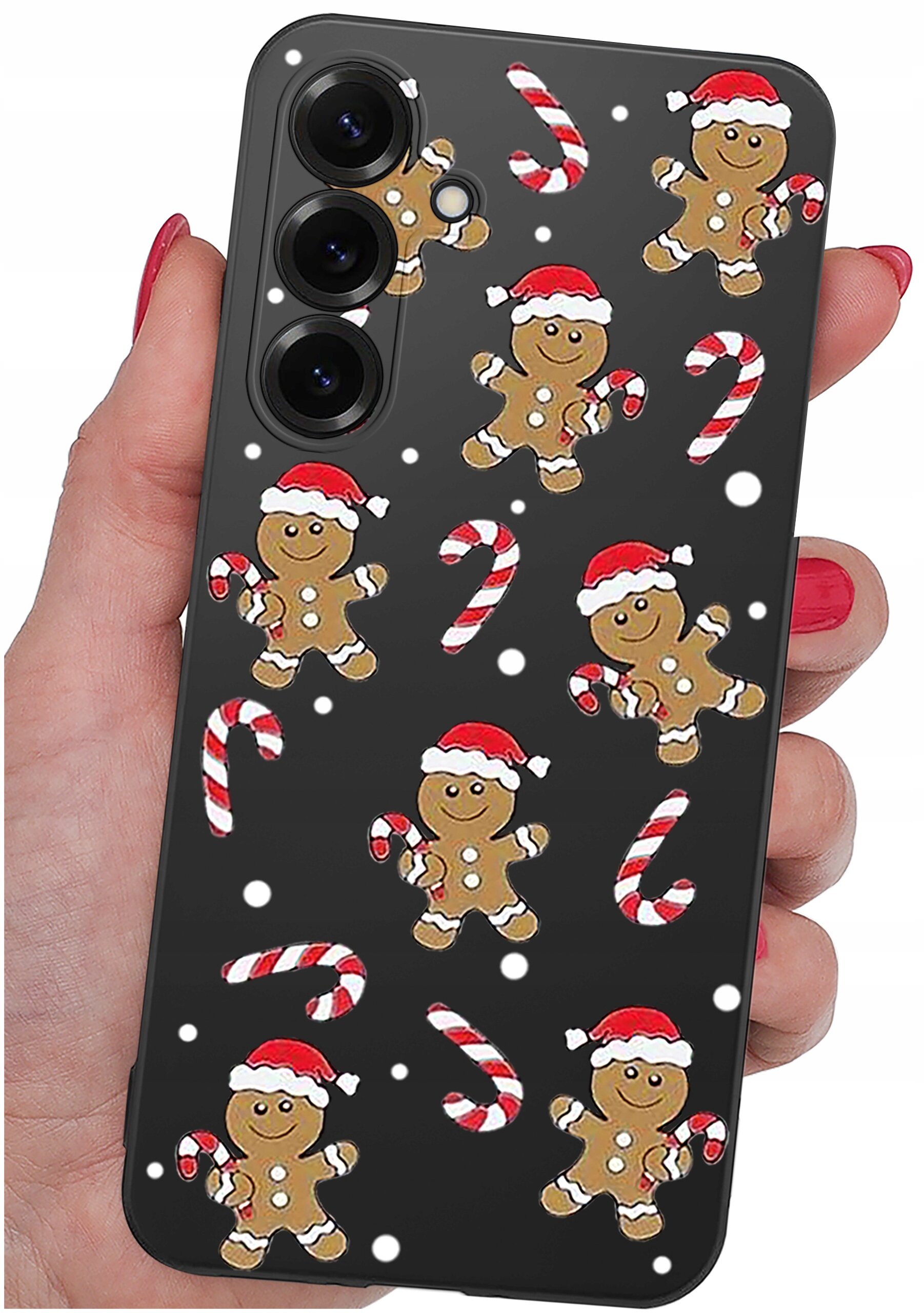 Etui na telefon z motywem świątecznym, przedstawiające piernikowe ludziki w czapkach Mikołaja oraz cukrowe laski na czarnym tle. Etui trzymane jest w dłoni z pomalowanymi na czerwono paznokciami.