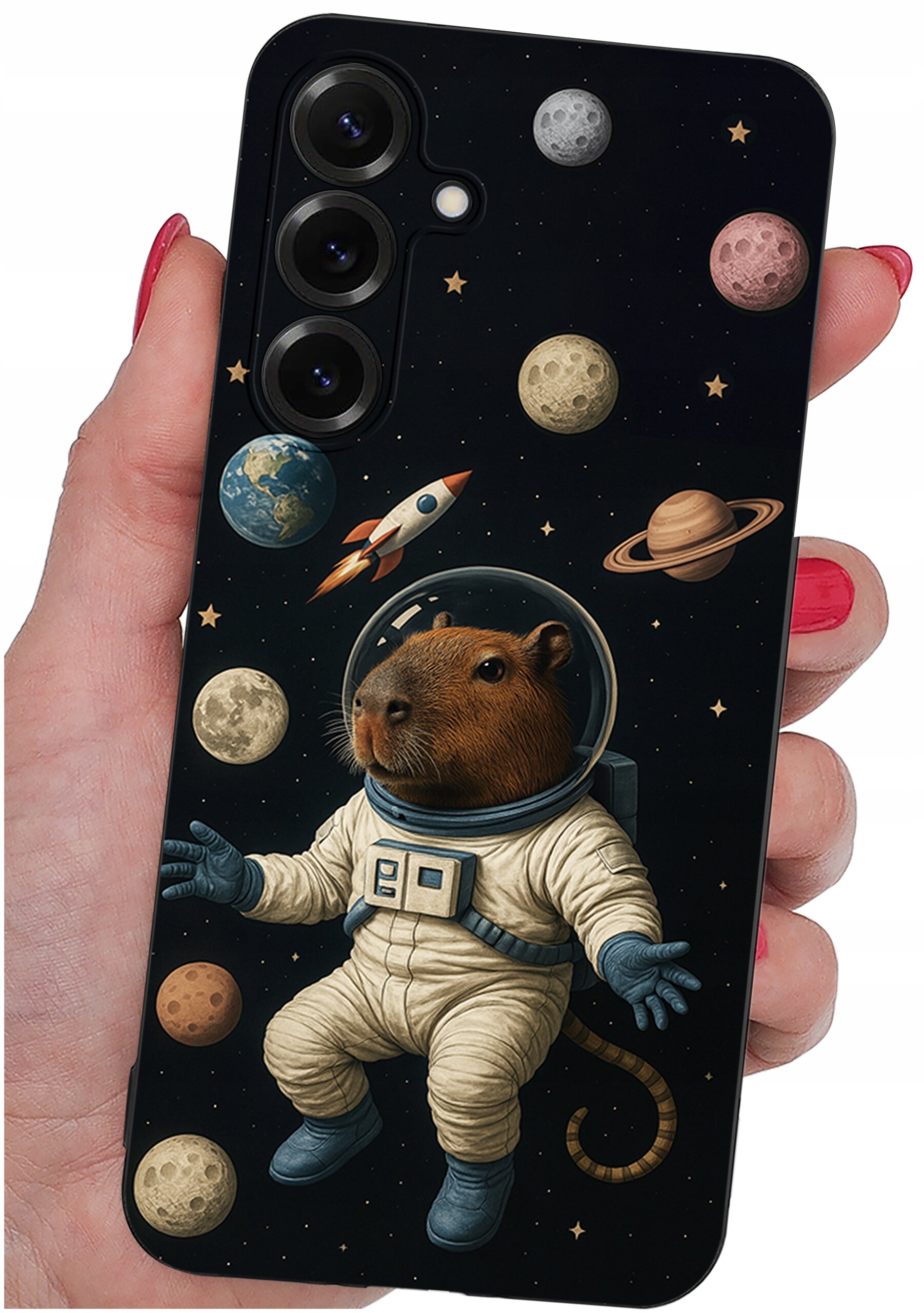 Etui na telefon z motywem kosmicznym, przedstawiające kapibarę w skafandrze astronauty otoczoną planetami i rakietą. Etui trzymane jest w dłoni z pomalowanymi na czerwono paznokciami.