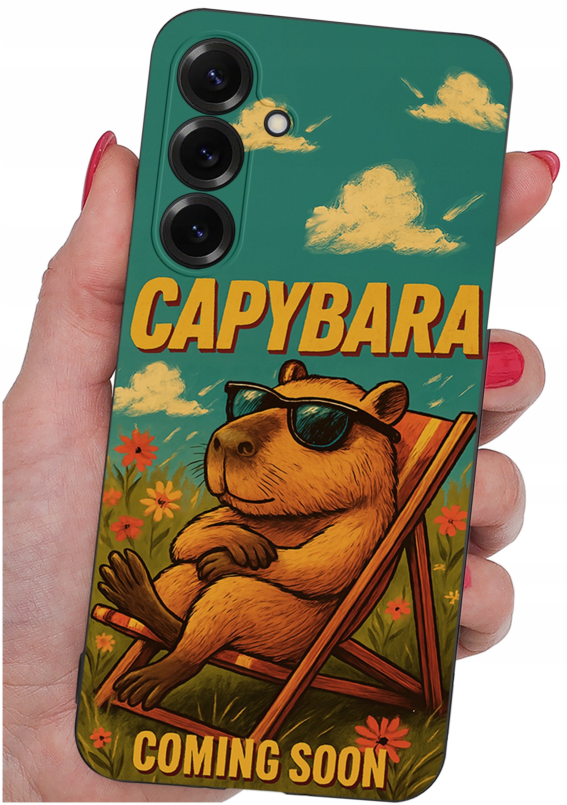 Etui na telefon z grafiką kapibary w okularach przeciwsłonecznych, siedzącej na leżaku wśród kwiatów. Na etui widnieje tekst: \'CAPYBARA COMING SOON\'.
