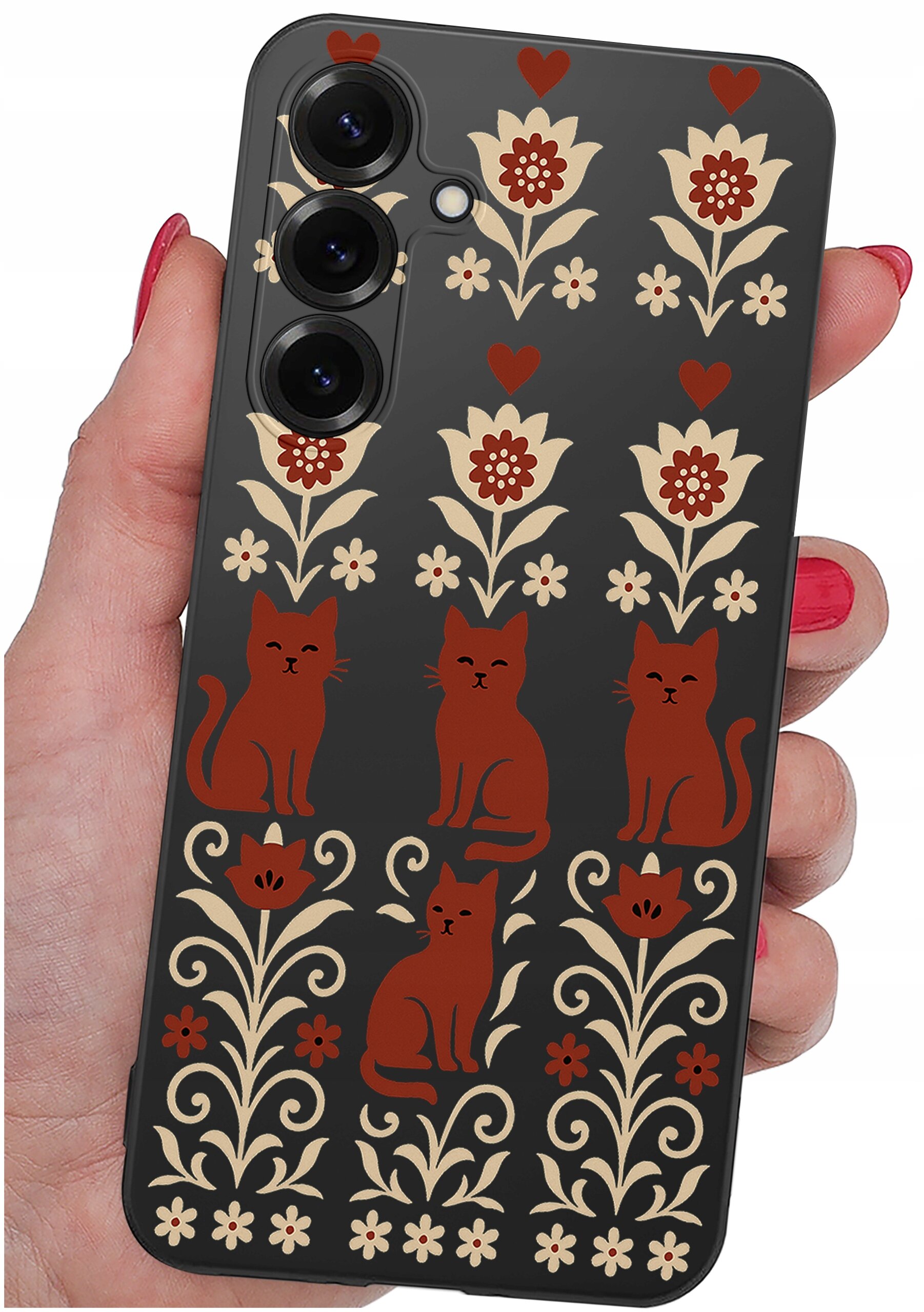 Etui na telefon z wzorem przedstawiającym czerwone koty i kwiaty na ciemnym tle. Etui trzymane jest w dłoni z pomalowanymi na czerwono paznokciami.