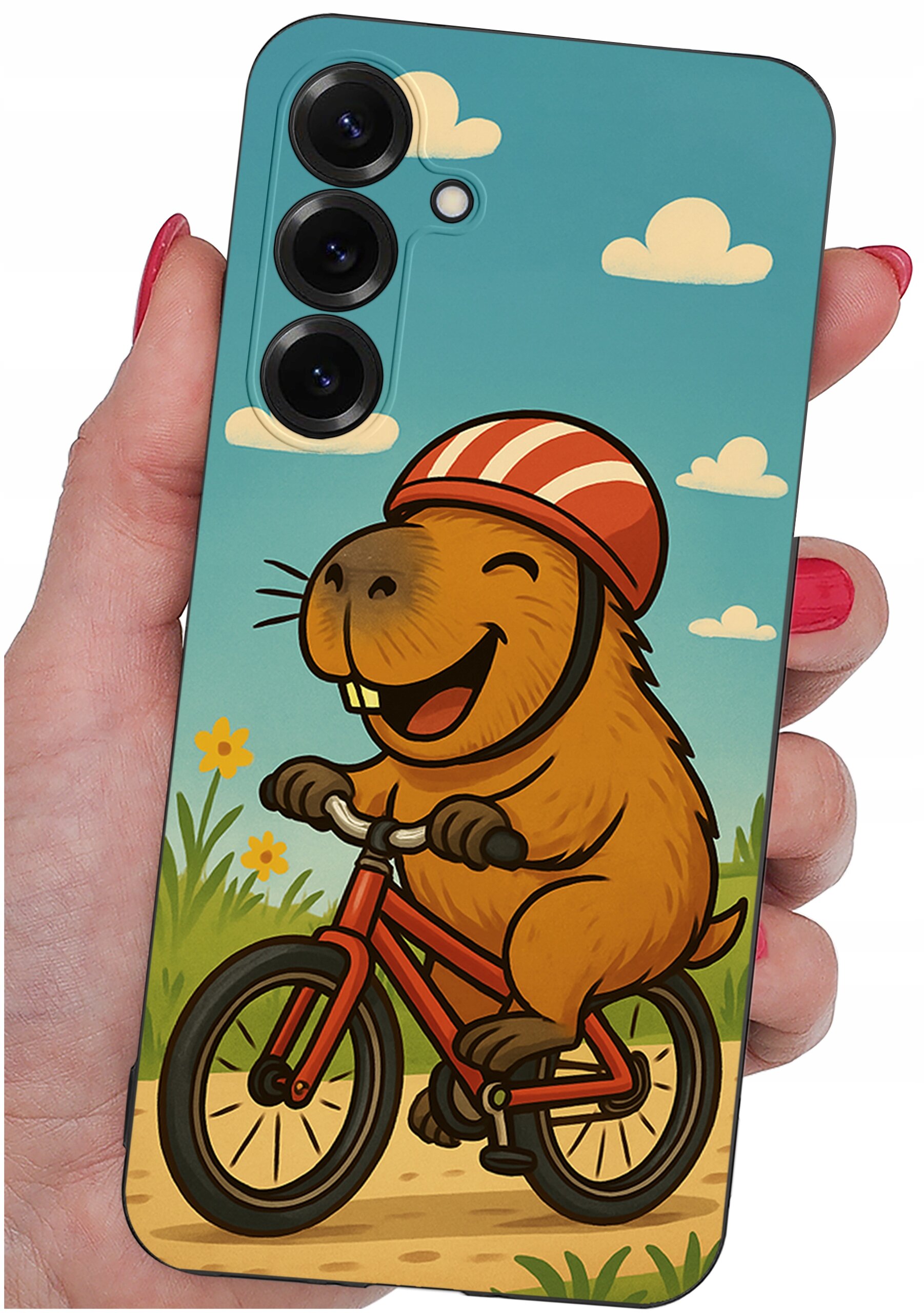 Etui na telefon z kolorowym nadrukiem przedstawiającym uśmiechniętego zwierzęcia na rowerze w kasku, na tle nieba z chmurkami i kwiatami. Etui trzymane jest w dłoni z pomalowanymi na czerwono paznokciami.