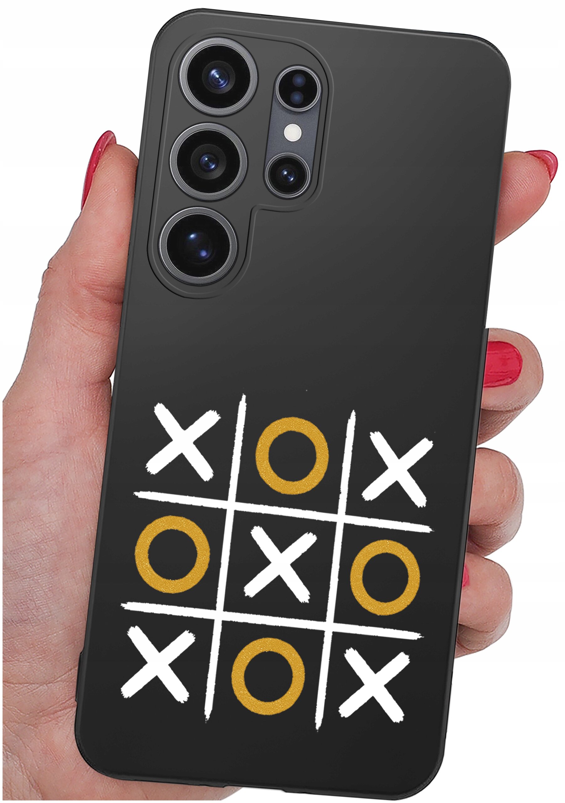 Czarna obudowa telefonu z wzorem gry w kółko i krzyżyk, gdzie kółka są złote, a krzyżyki białe. Obudowa jest trzymana w dłoni z pomalowanymi na czerwono paznokciami.