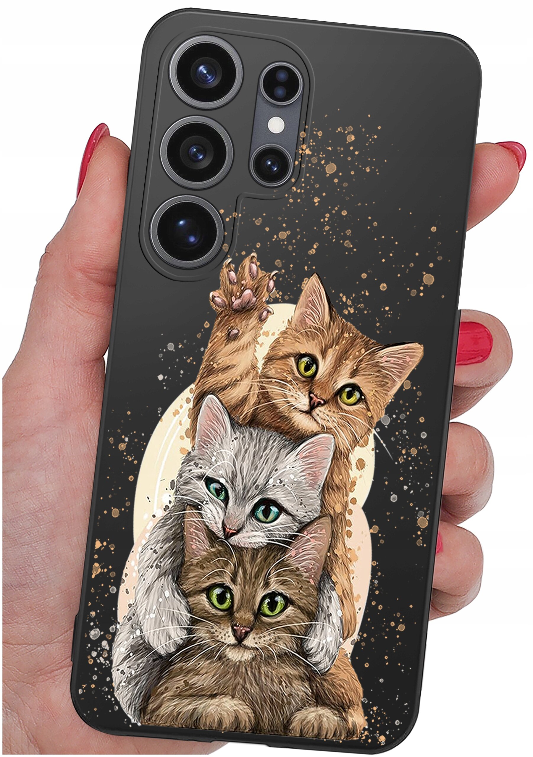 Etui na telefon z trzema rysunkowymi kotami na ciemnym tle, trzymane w dłoni z czerwonym lakierem na paznokciach. W tle widoczne są złote plamki dekoracyjne.