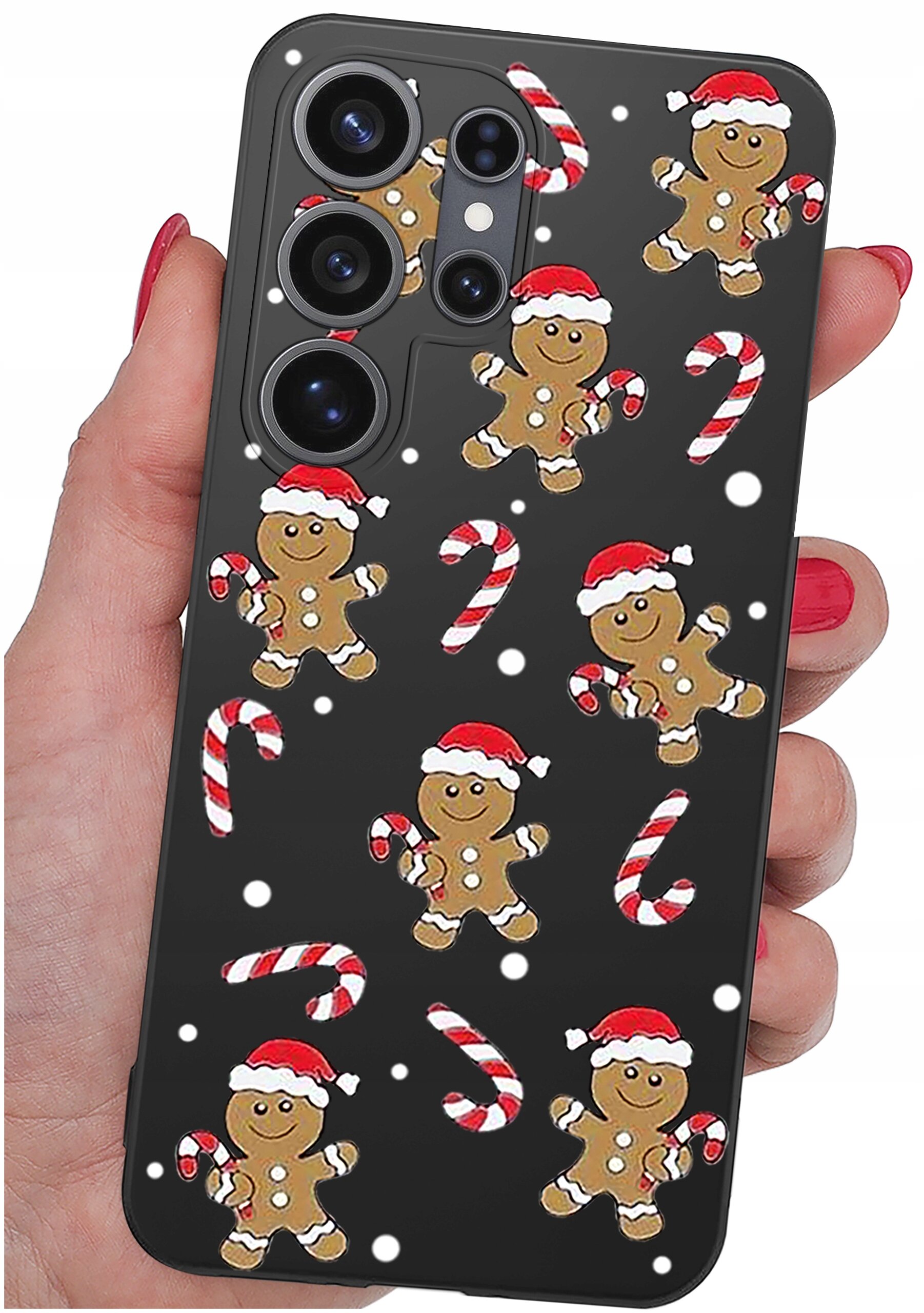 Etui na telefon z motywem świątecznym, przedstawiające piernikowe ludziki w czapkach Mikołaja oraz cukrowe laski na czarnym tle. Etui trzymane jest w dłoni z pomalowanymi na czerwono paznokciami.