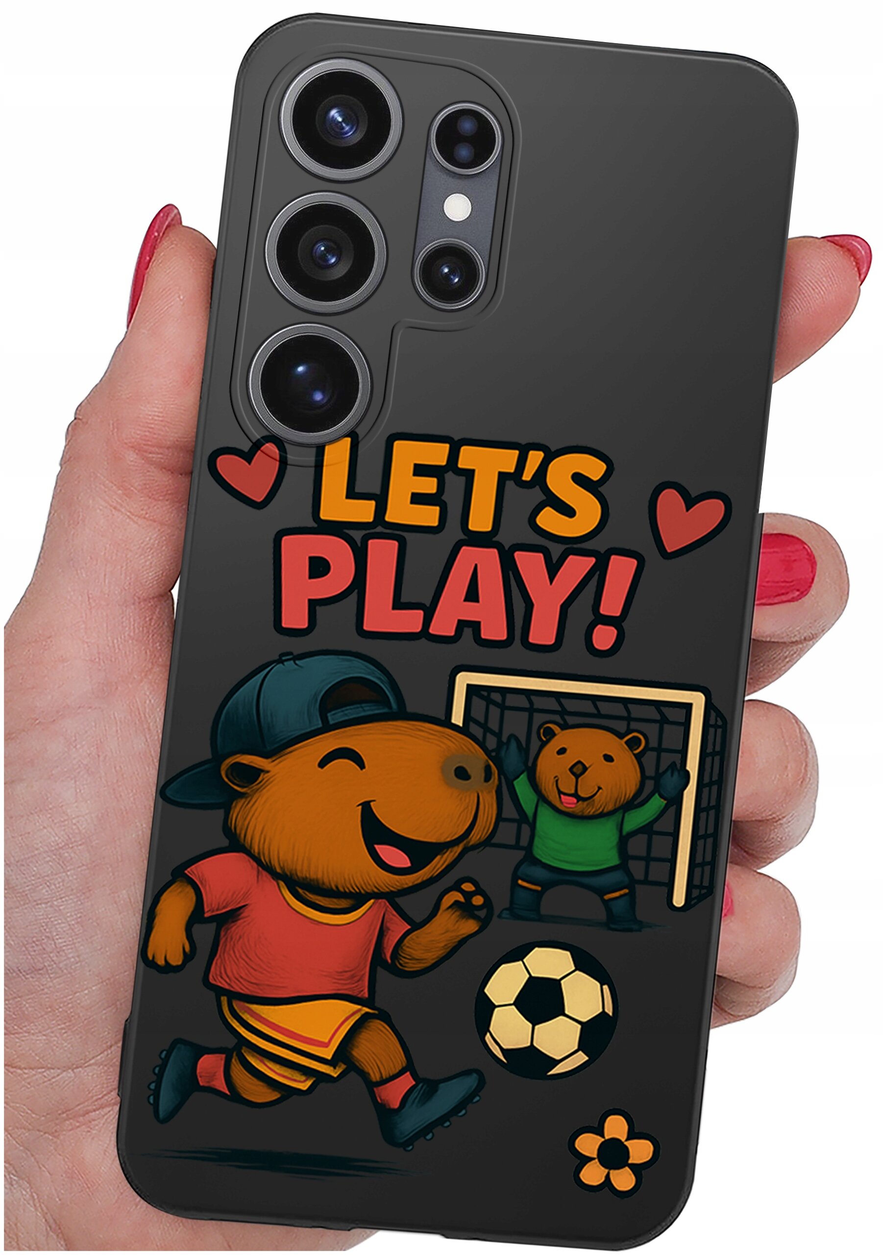 Etui na telefon z grafiką przedstawiającą zwierzęta grające w piłkę nożną oraz napis \'LET\'S PLAY!\' otoczony sercami. Etui jest trzymane w dłoni z pomalowanymi na czerwono paznokciami.