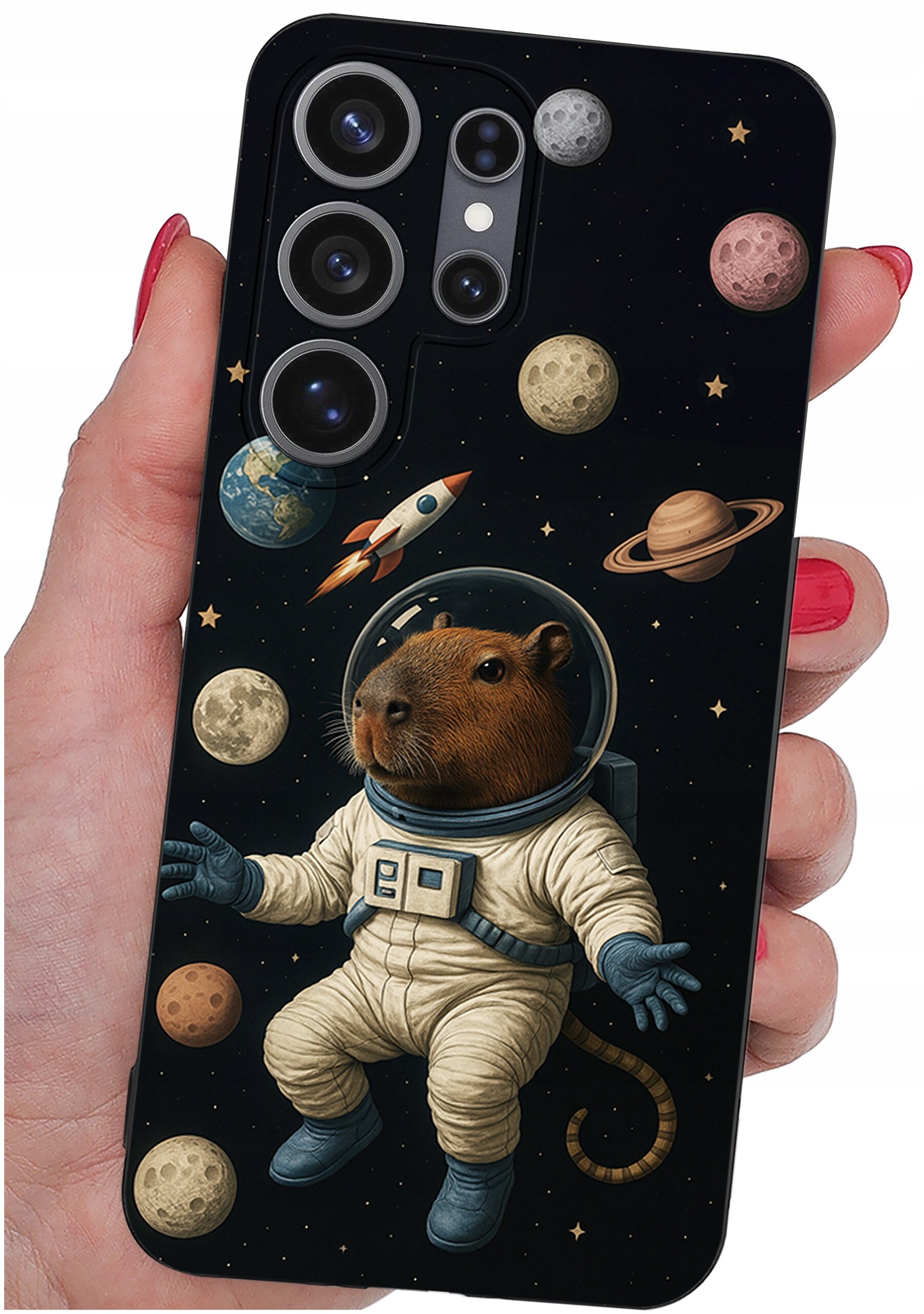Etui na telefon z grafiką przedstawiającą kapibarę w skafandrze kosmicznym, otoczoną planetami i rakietą na tle gwiazd. Etui trzymane jest w dłoni z pomalowanymi na czerwono paznokciami.