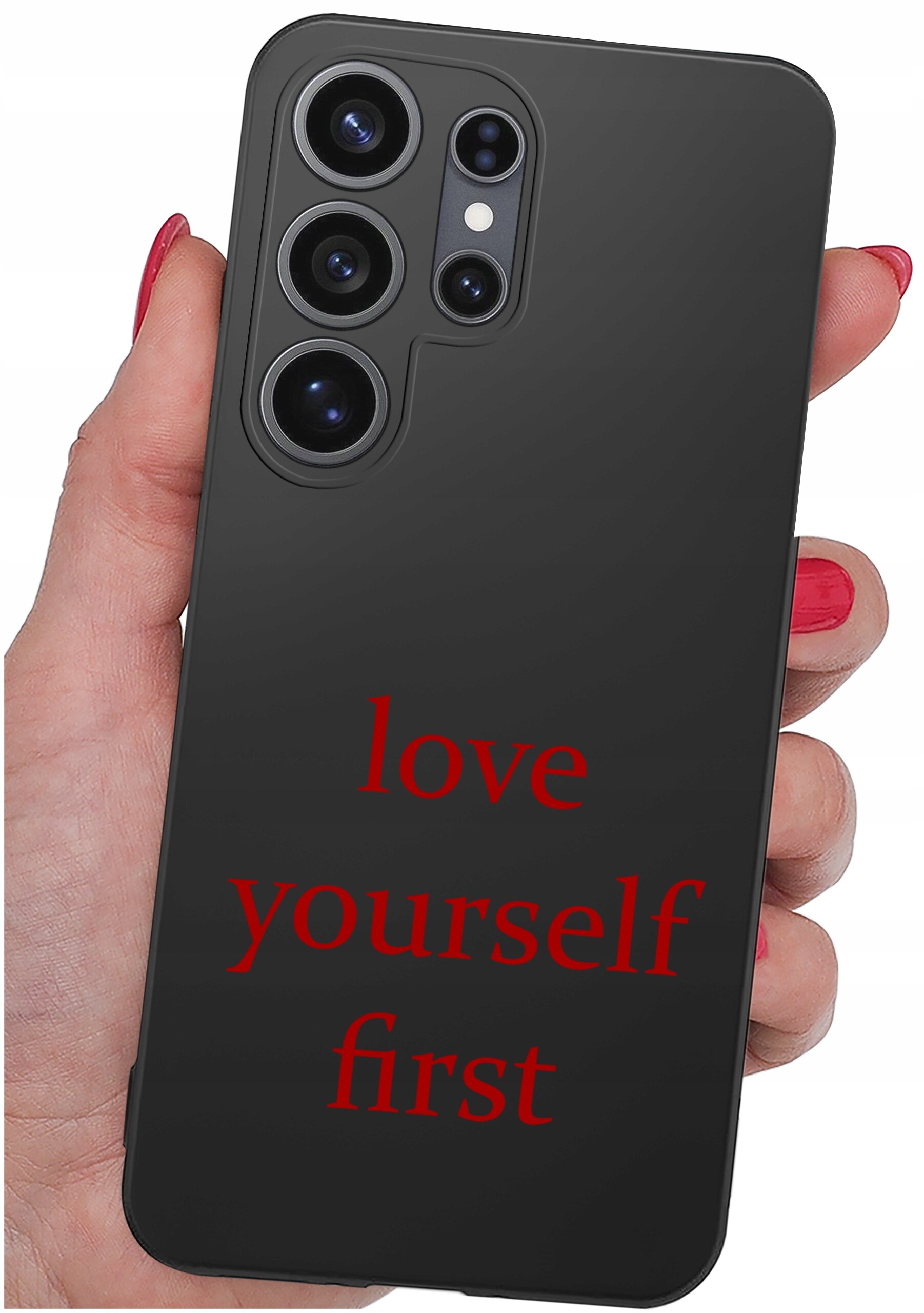 Czarna obudowa telefonu z trzema dużymi obiektywami aparatu i napisem \'love yourself first\' w czerwonym kolorze. Obudowa jest trzymana w dłoni z pomalowanymi na czerwono paznokciami.