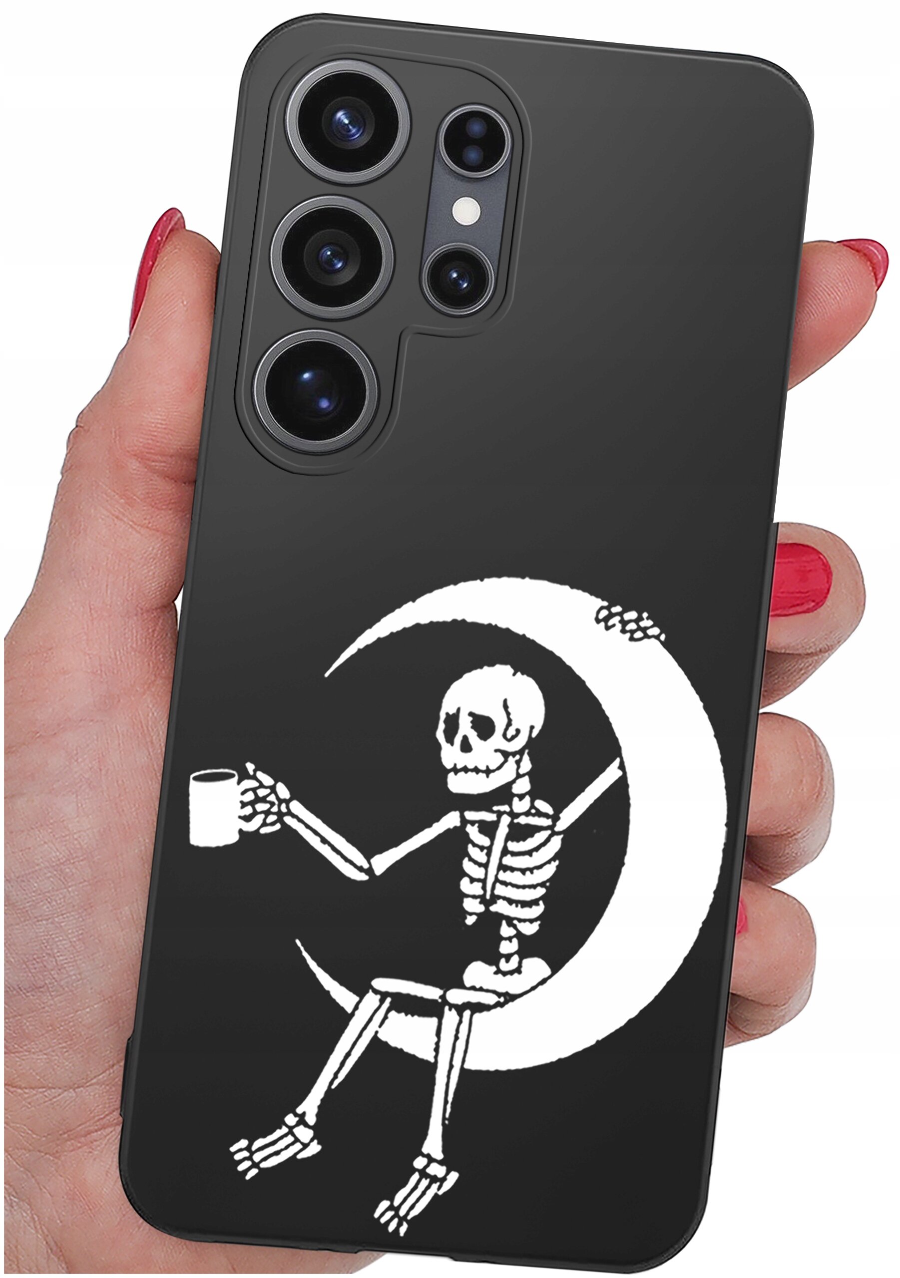 Czarne etui na telefon z nadrukiem białego szkieletu siedzącego na księżycu, trzymającego kubek. Etui jest trzymane w dłoni z pomalowanymi na czerwono paznokciami.