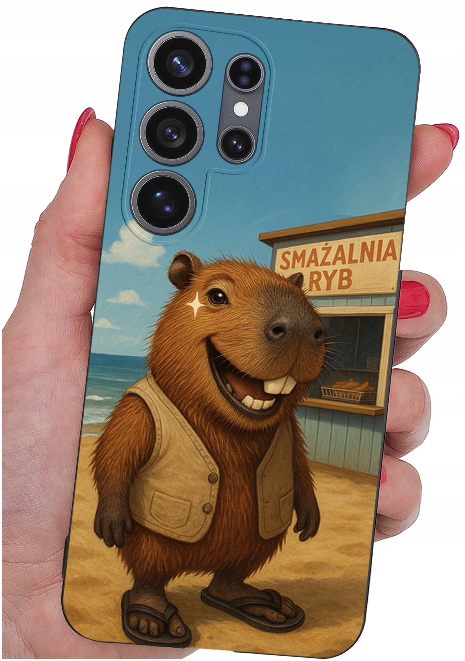 Etui na telefon z grafiką przedstawiającą uśmiechniętą kapibarę w kamizelce i klapkach, stojącą na plaży. W tle widoczny jest budynek z napisem \'SMAŻALNIA RYB\'.